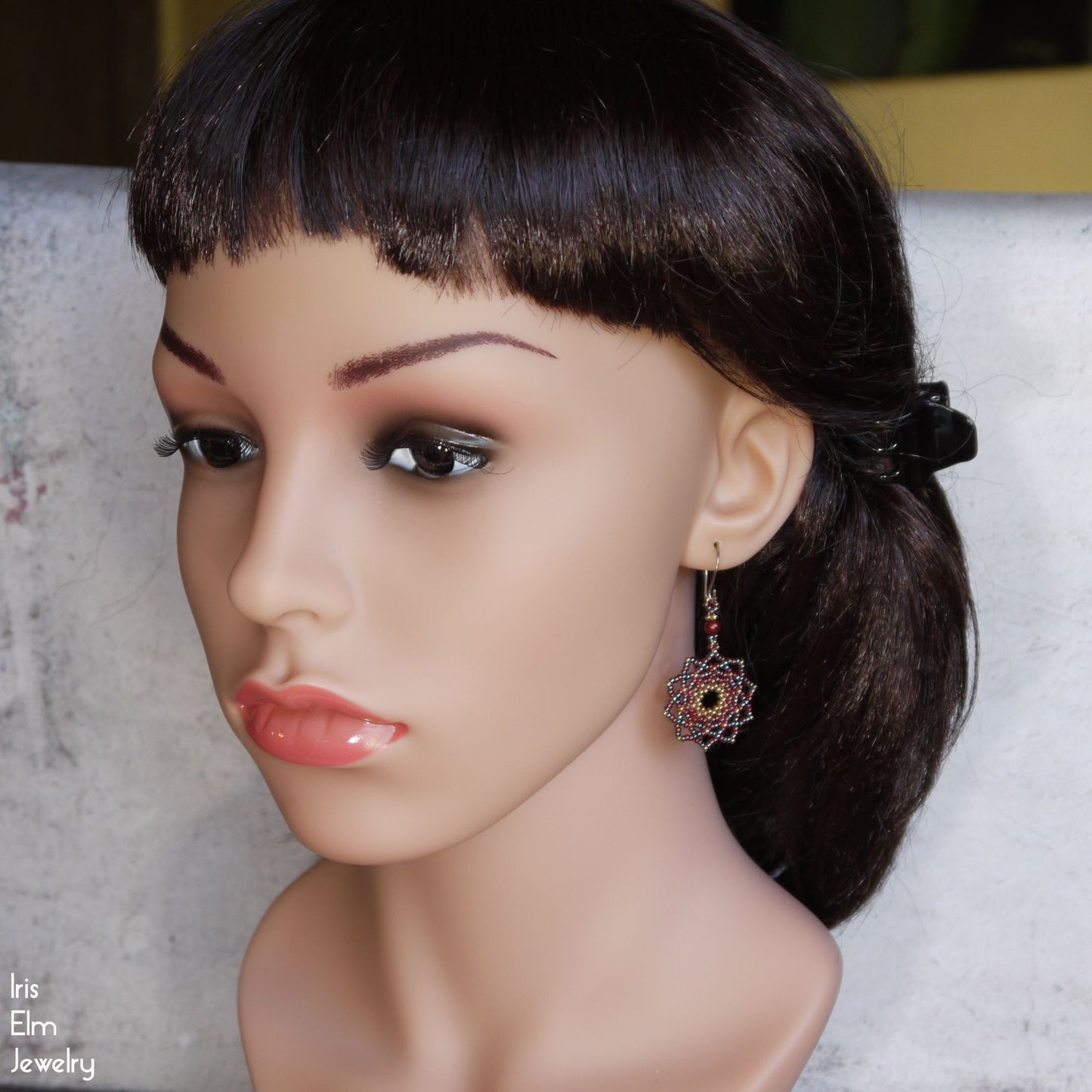 Mannequin head with a stylish hairstyle and red mandala earrings on a neutral background