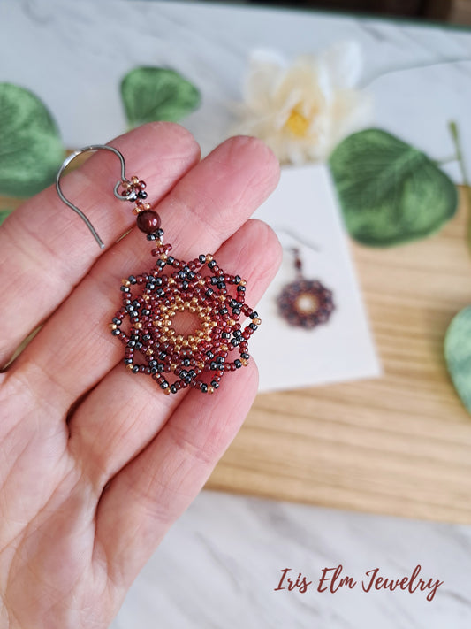 hand holding a red and golden glass seed bead woven mandala earring. Iris Elm Jewelry