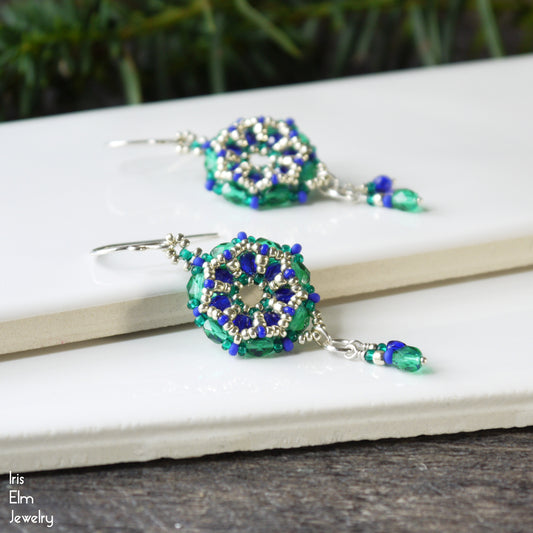 Pair of green and blue beaded Czech glass earrings on a white surface with a blurred natural background.