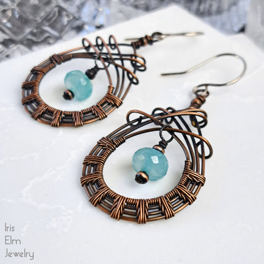 Pair of copper wire-wrapped earrings with chalcedony light blue stone beads on a white surface.