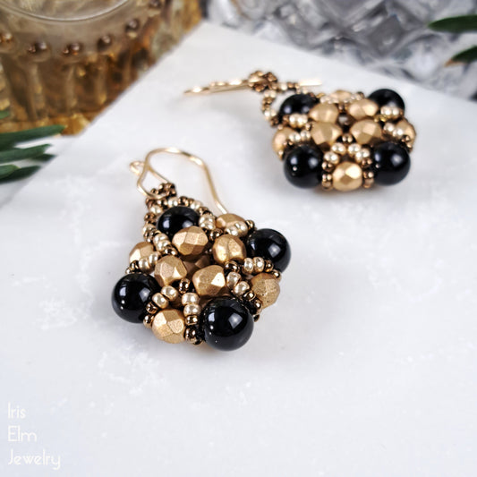 Pair of gold glass and black onyx beaded earrings on a white surface with a blurred background.