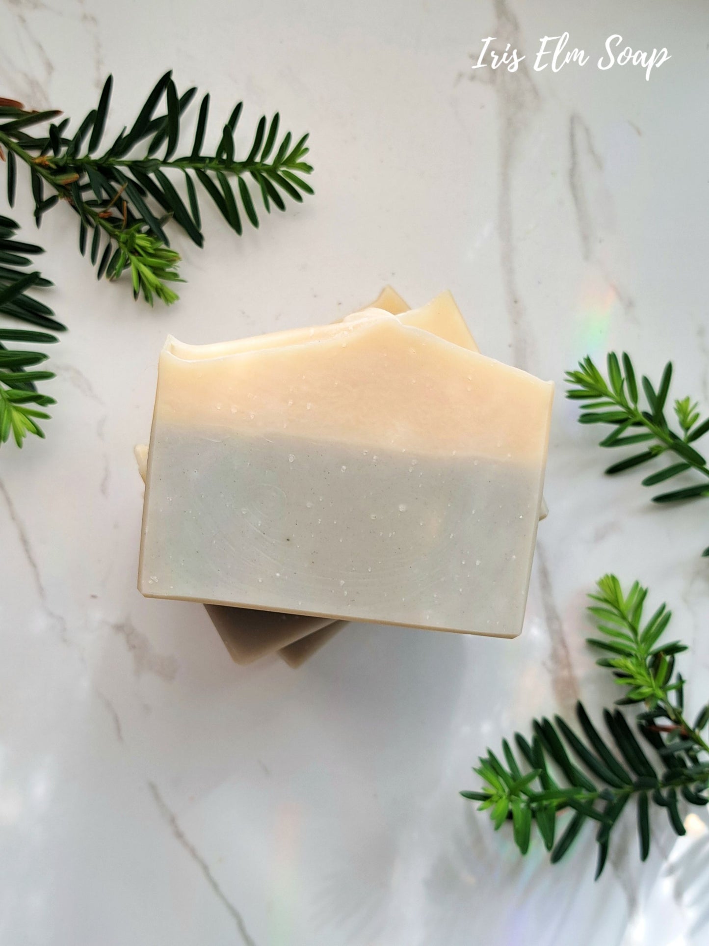 Two bars of cedarwood calm essential oil soap on a marble surface with greenery, featuring 'Iris Elm Soap' branding.