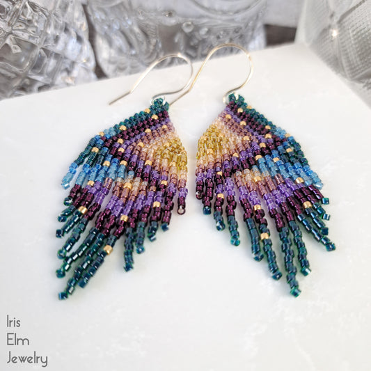 Multicolored beaded rainbow fringe handmade seed bead earrings on a white surface with 'Iris Elm Jewelry' branding.