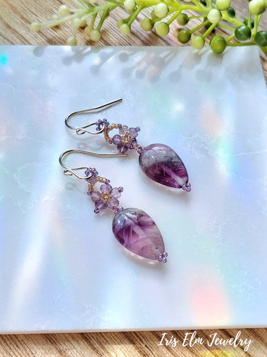 purple amethyst beaded flower and rainbow fluorite leaf gemstone dangle earrings on white marble surface