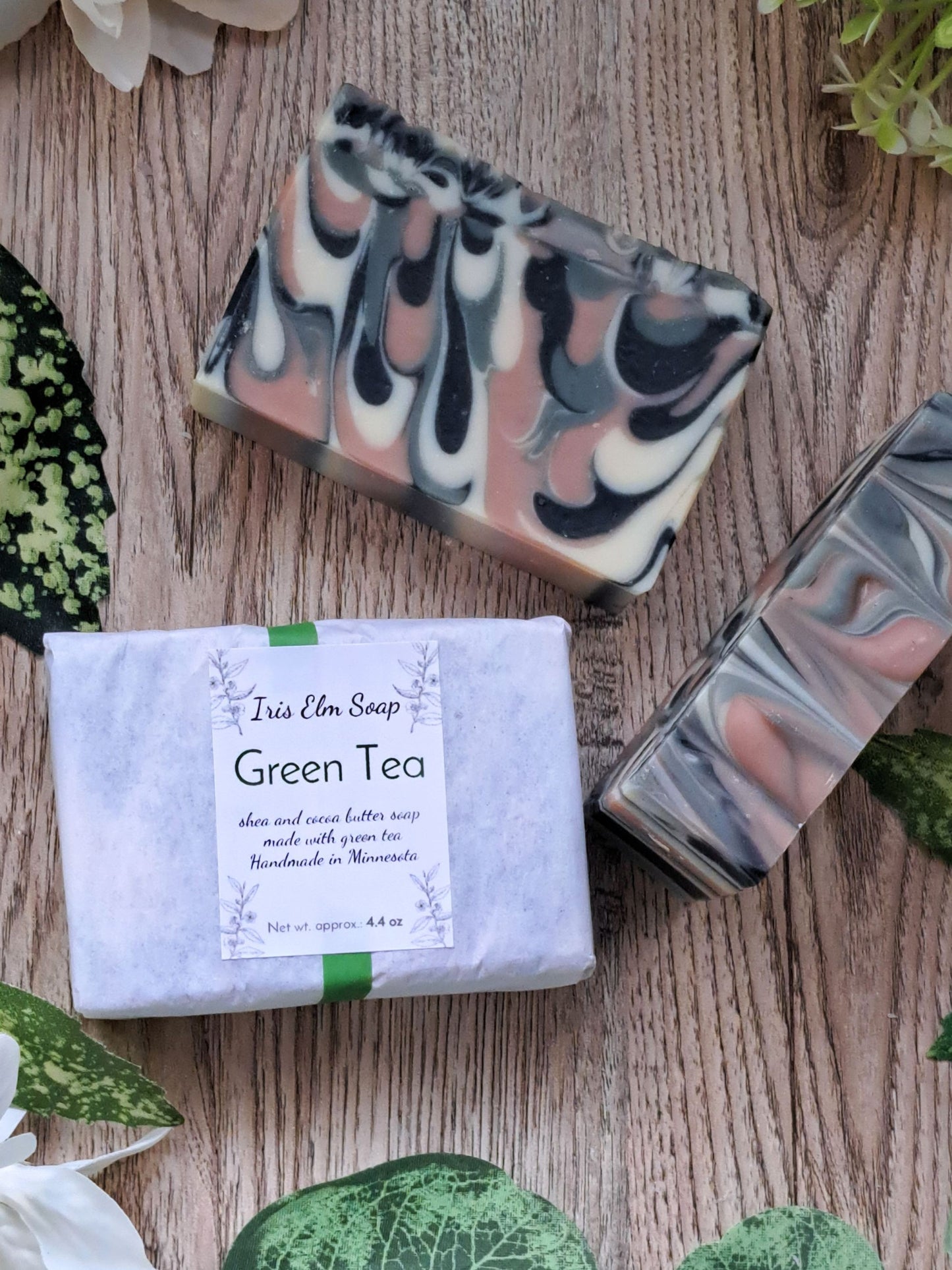 Three bars of soap with a 'Green Tea' label on a wooden surface with green leaves.