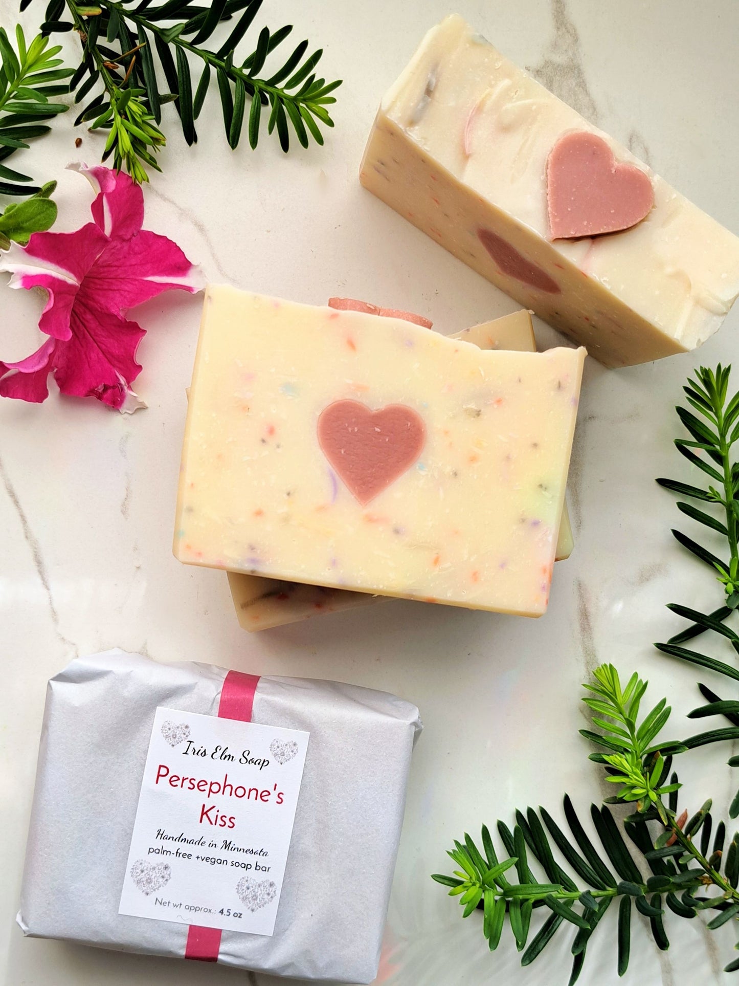 Three bars of persephone's kiss handmade spring goddess soap with heart designs on a marble surface with greenery and flowers.