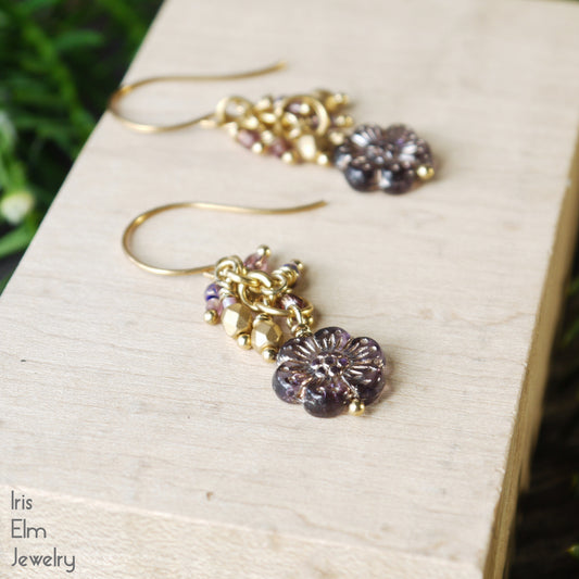 Gold and purple floral glass cluster earrings on a wooden surface with 'Iris Elm Jewelry' branding.