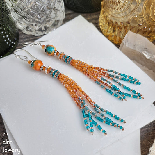 Beaded ocean jade and carnelian tassel earrings with orange and teal seed beads on a white surface, with 'Iris Elm Jewelry' branding.