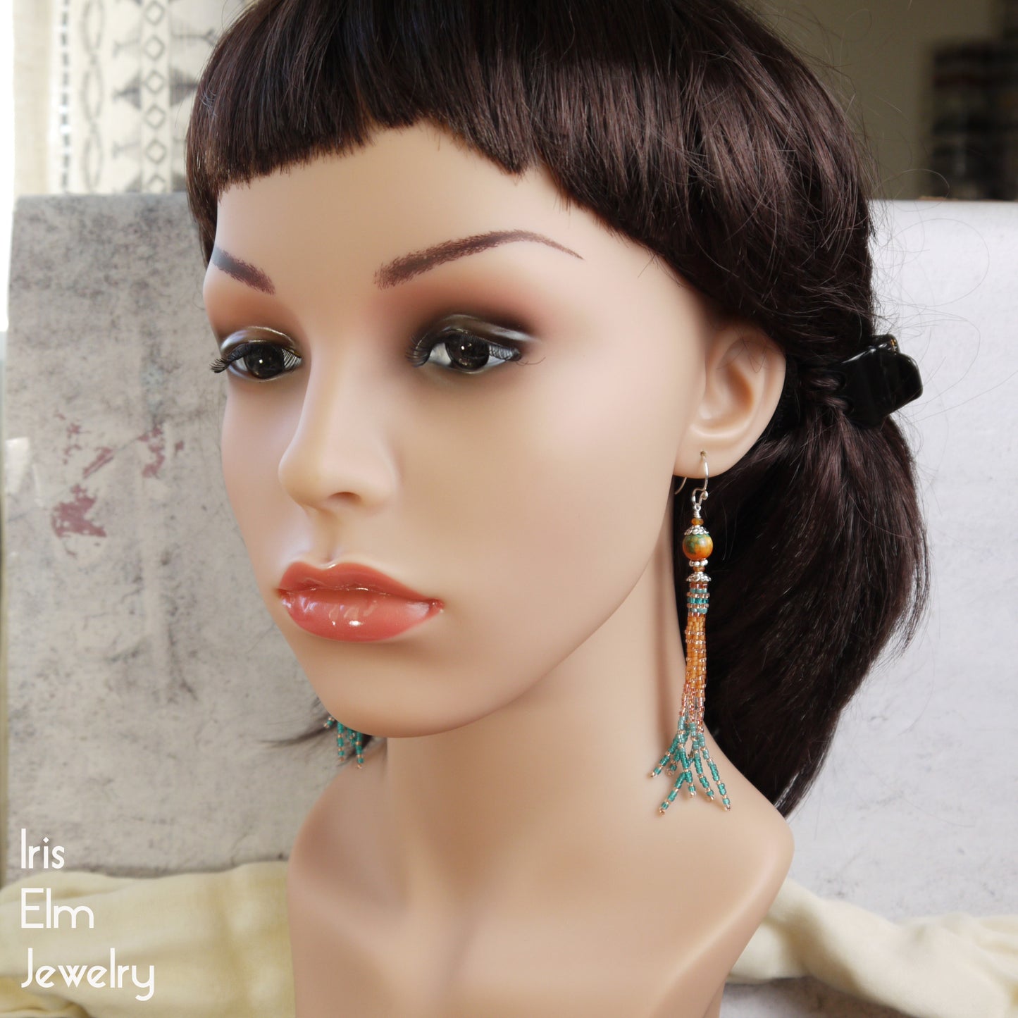 Mannequin head with a pair of ocean jade and carnelian tassel earrings on a neutral background