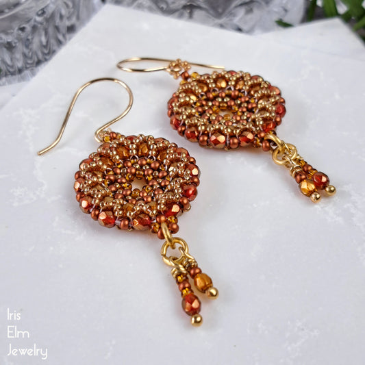 Pair of beaded earrings with gold and orange beads on a white surface.