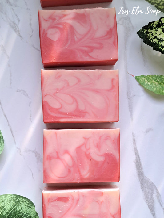 Pink marbled peach bellini handmade soap bars on a white surface with green leaves.