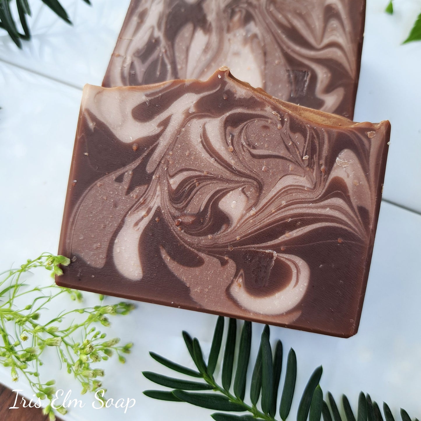 Swirl patterned vanilla handmade soap bars on a white surface with green leaves