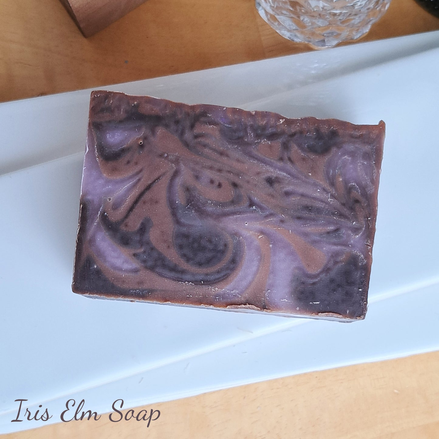 Swirled purple and brown black amber and lavender handmade soap bar on a white plate with 'Iris Elm Soap' branding.