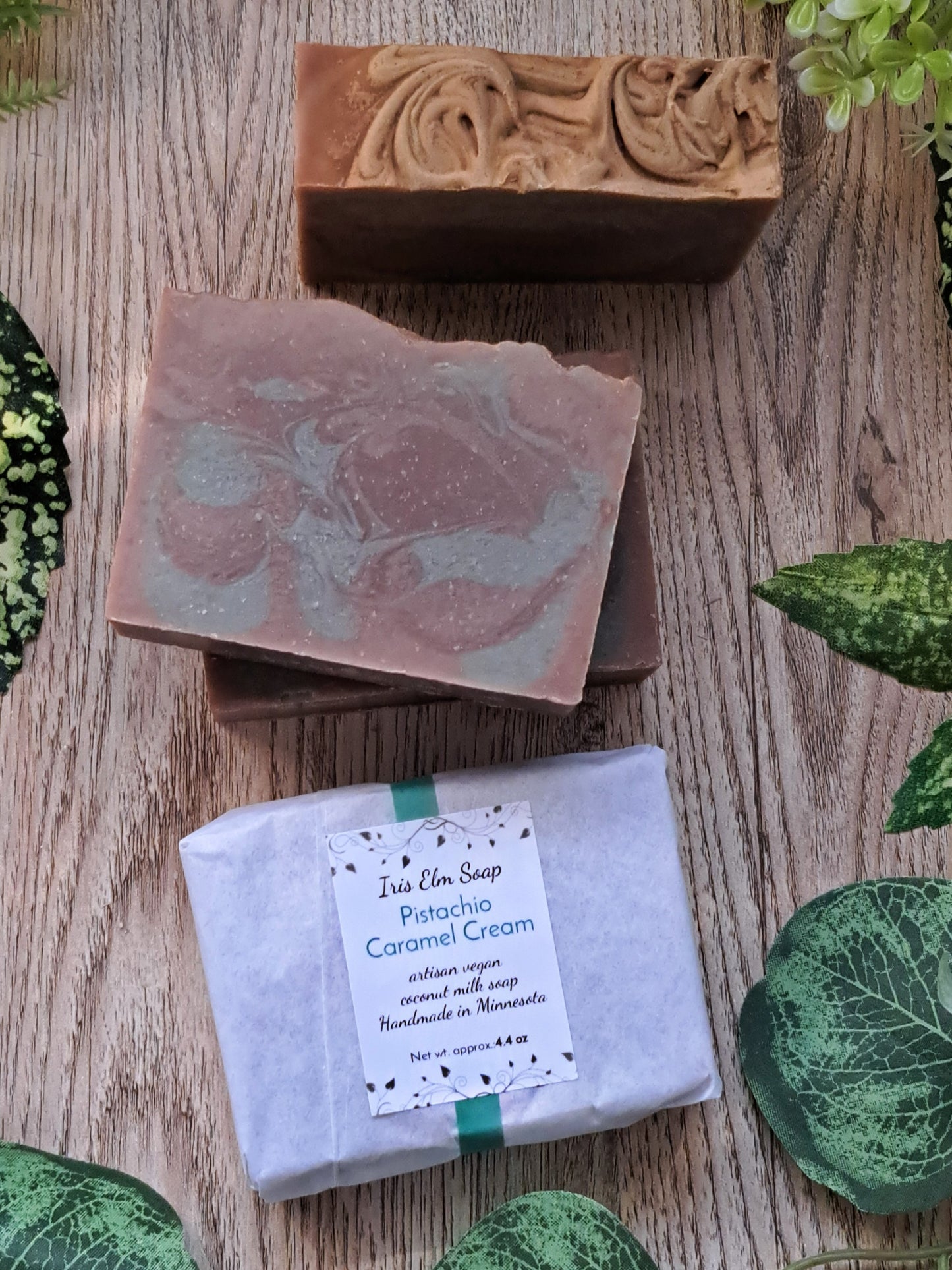 Three pistachio caramel cream handmade soap bars on a wooden surface with greenery