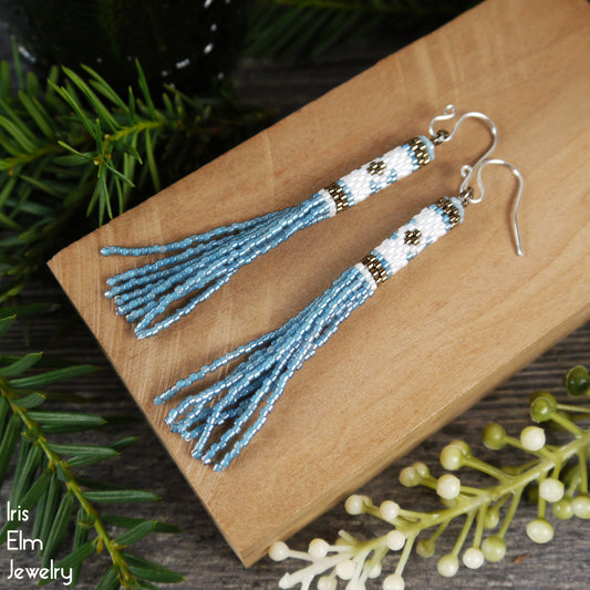 Blue tassel seed bead earrings on a wooden surface with greenery