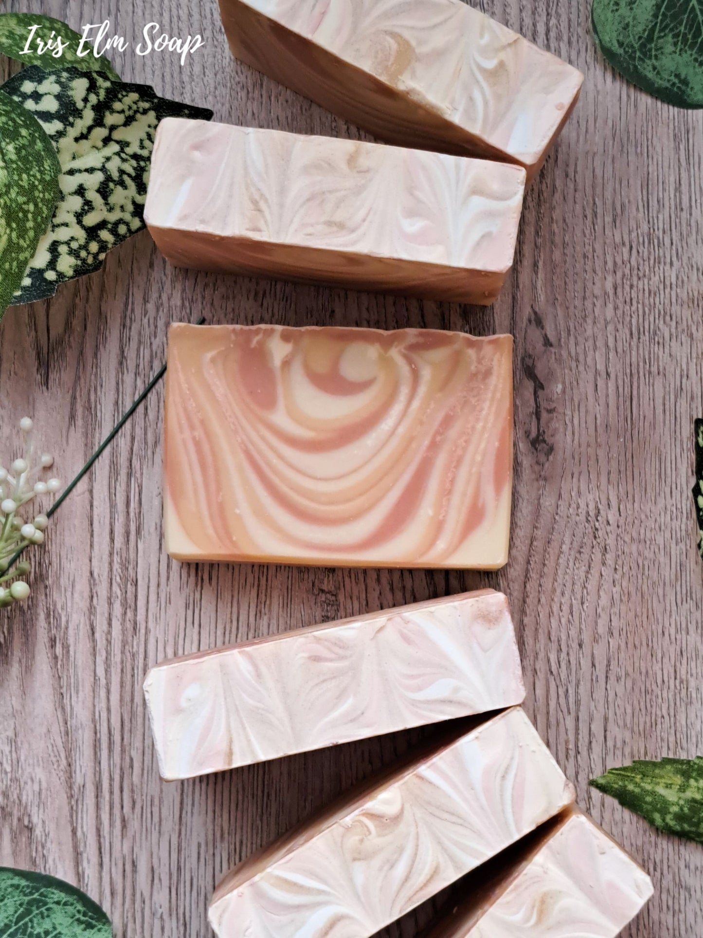 Marbled mango tangerine handmade tropical scented soap bars on a wooden surface with green leafy elements.