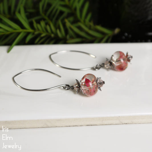 pink wildflowers in resin drop stainless steel marquise earrings on a white surface with greenery in the background
