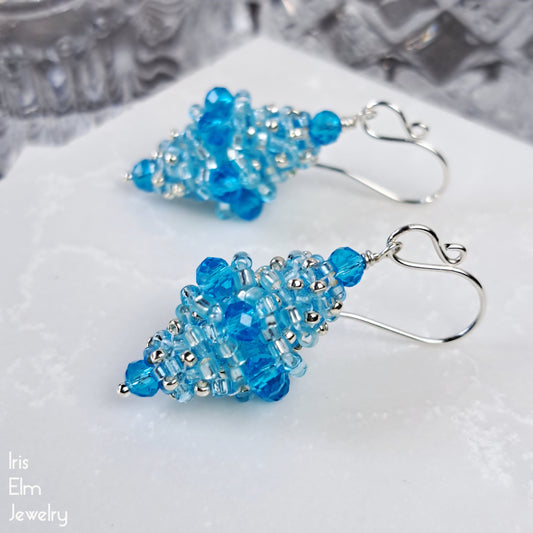 light blue faceted glass beaded bead sterling silver earrings on a white surface with a blurred background