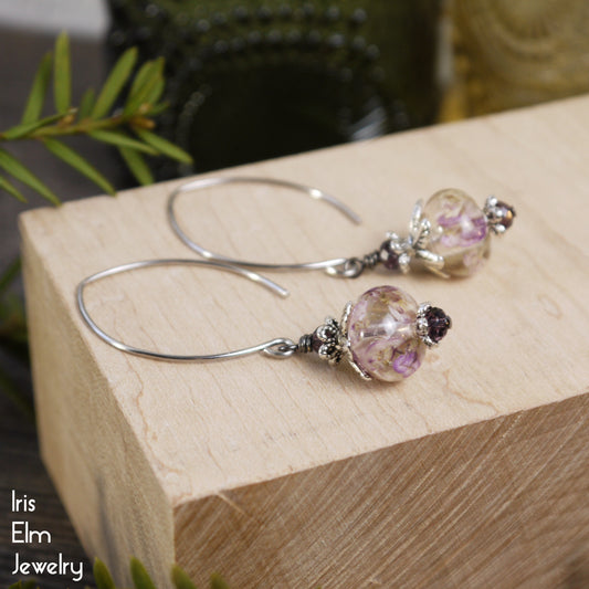 real flower marquise drop earrings with purple and clear beads on a wooden block, brand 'Iris Elm Jewelry' visible.