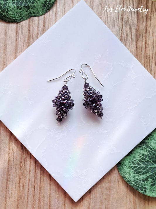 Pair of purple beaded bead glass earrings on a white napkin with green leaves on a wooden surface