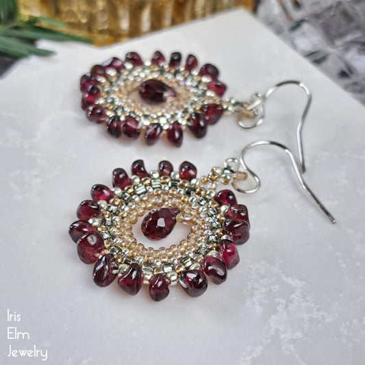 Pair of beaded earrings with red garnet and gold beads on a white surface, branded 'Iris Elm Jewelry'.