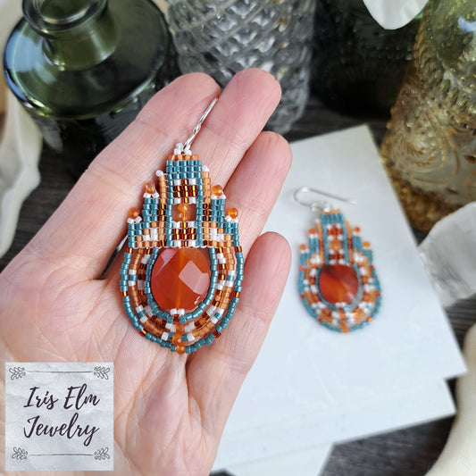 Beaded carnelian teardrop earrings held in a hand with 'Iris Elm Jewelry' card in the background