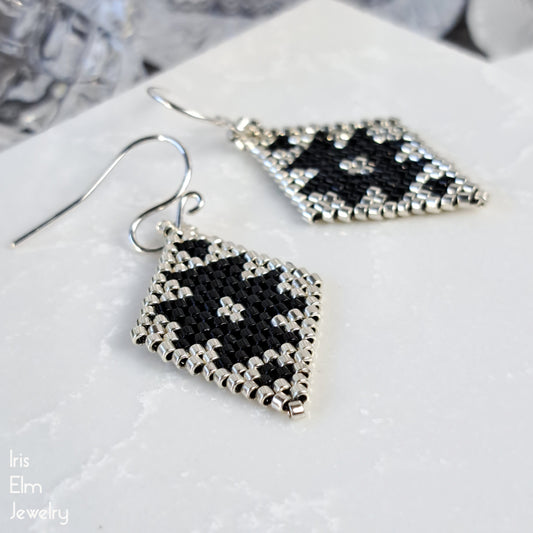 Black and silver southwestern geometric seed bead earrings on a white surface with 'Iris Elm Jewelry' branding.