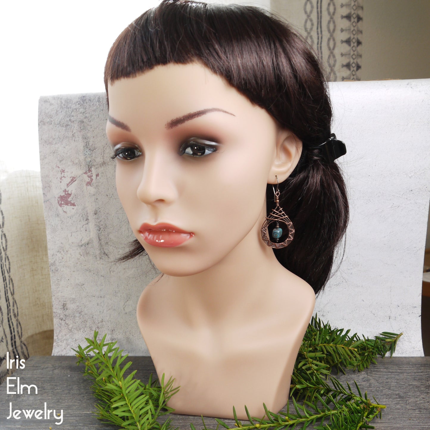 Mannequin head with dark hair and jasper copper teardrop earrings on a decorative background