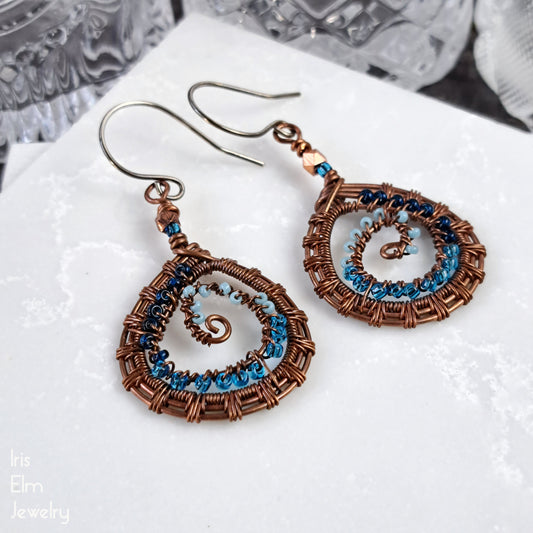 Pair of copper wire wrapped spiral earrings with blue accents on a white surface