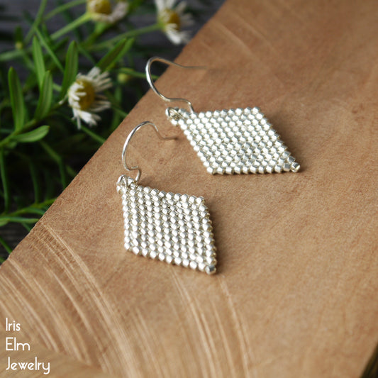 Silver geometric glass seed bead diamond earrings on a wooden surface with a natural background
