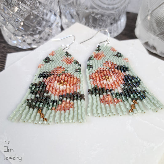 Beaded mint green and peach Victorian rose seed bead fringe earrings with intricate design on a white napkin, branded 'Iris Elm Jewelry'.