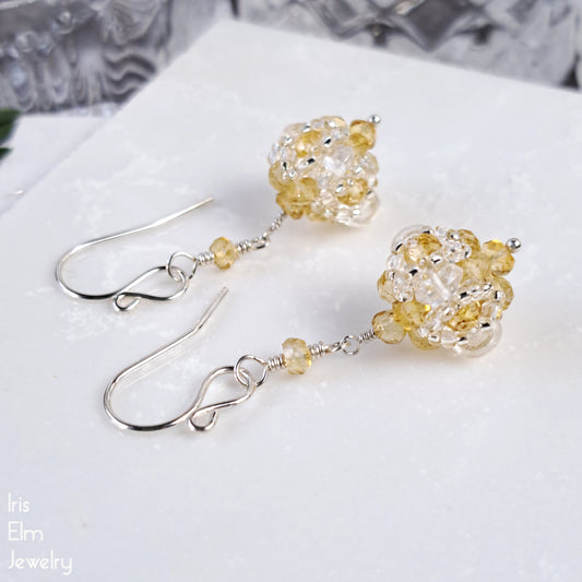 Pair of beadwork gemstone earrings with yellow citrine and clear quartz crystal bead drops on a white surface.