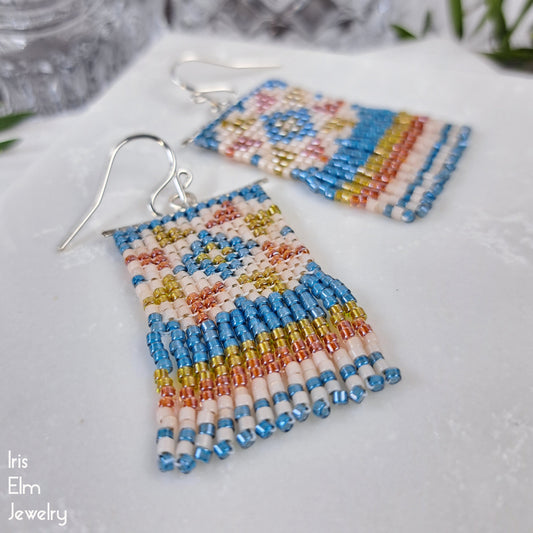 Colorful beaded blue, orange, and yellow seed bead quilt fringe earrings on a white surface with 'Iris Elm Jewelry' branding.