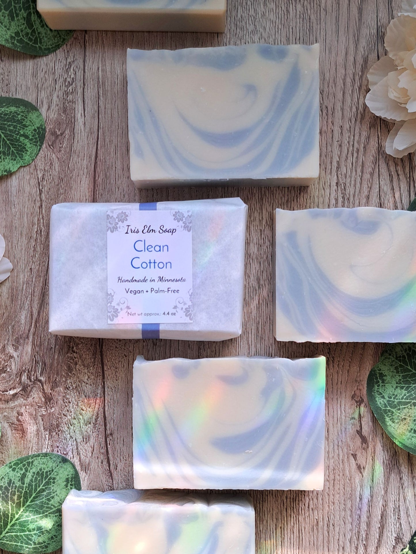 Handmade soap bars with 'Clean Cotton' label on a wooden surface with green leaves.