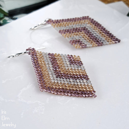 Beaded grey, pink, and golden chevron diamond shape seed bead earrings on a white surface with 'Iris Elm Jewelry' branding.