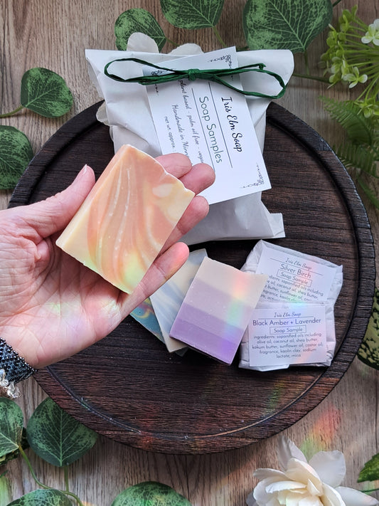 Hand holding a handmade cold process vegan soap bar with Iris Elm Soap samples on a wooden tray.