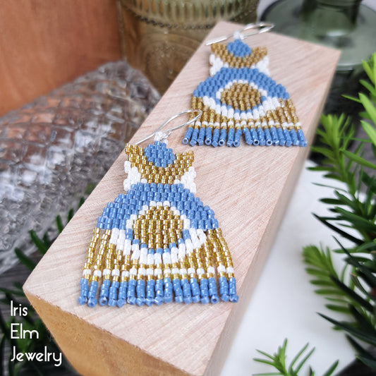 Pair of beaded blue, yellow, and white half circle seed bead modern fringe earrings on a wooden block with 'Iris Elm Jewelry' branding.