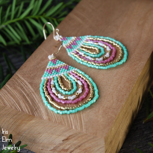 Colorful mint green, pink, and gold beaded seed bead teardrop earrings on a wooden surface with 'Iris Elm Jewelry' branding.