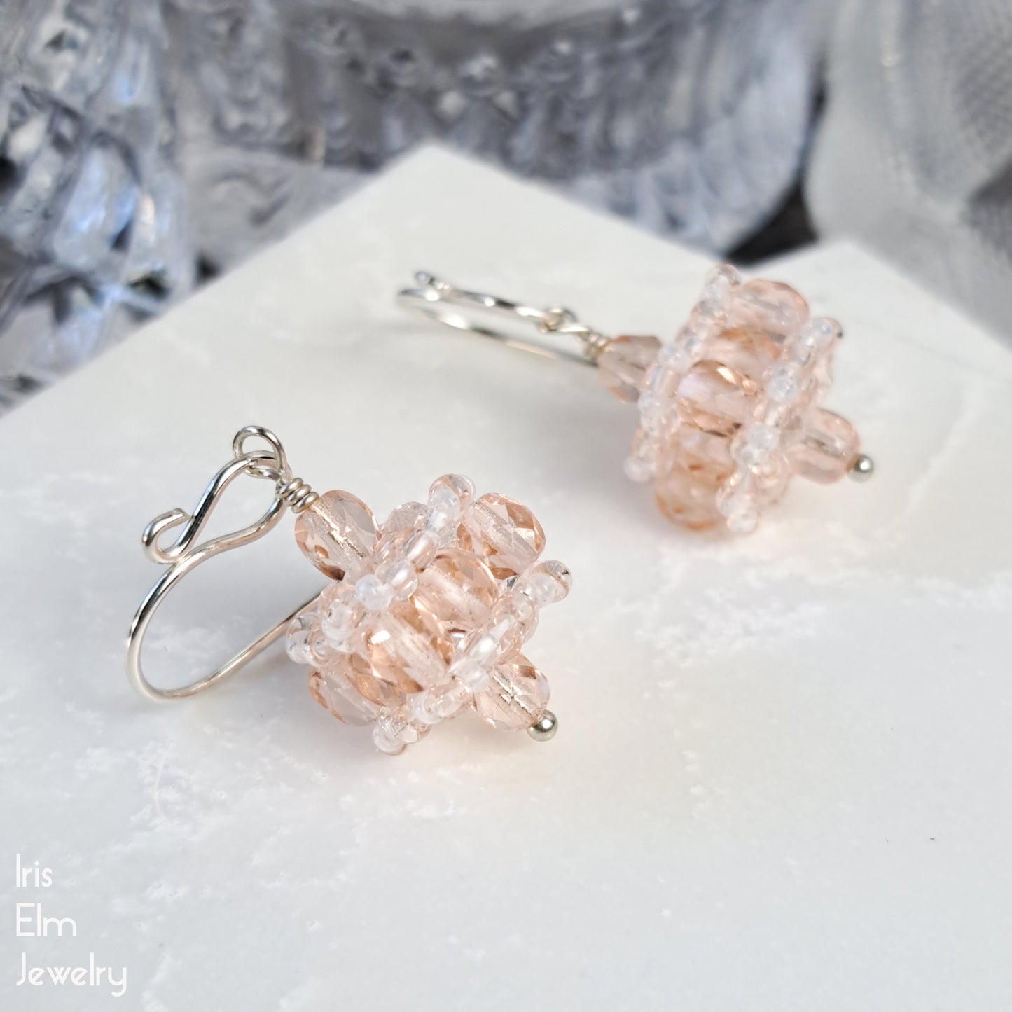 Pair of pale pink beaded earrings on a white surface with 'Iris Elm Jewelry' branding.