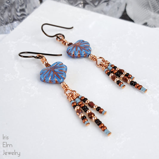 Pair of beaded leaf glass earrings with sead bead dangles and niobium ear wires on a white surface.
