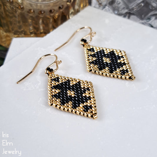 Gold and black beaded diamond shape earrings with southwestern design on a white surface with 'Iris Elm Jewelry' branding.
