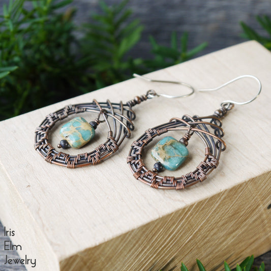 Pair of wire-wrapped teardrop earrings with aqua terra jasper square stones on a wooden block with greenery in the background.