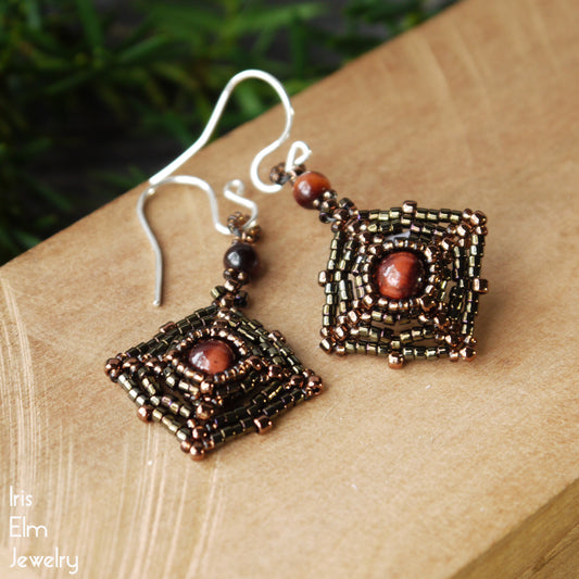 Pair of brown beaded square earrings with red tiger eye stones on a wooden surface, branded 'Iris Elm Jewelry'.