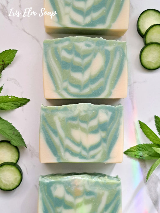 Green and white swirled garden mint and cucumber handmade soap bars with cucumber slices and mint leaves on a light background
