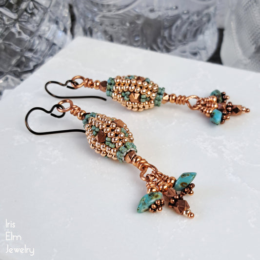 Pair of glass lantern beaded earrings with turquoise and copper colors on a white surface.