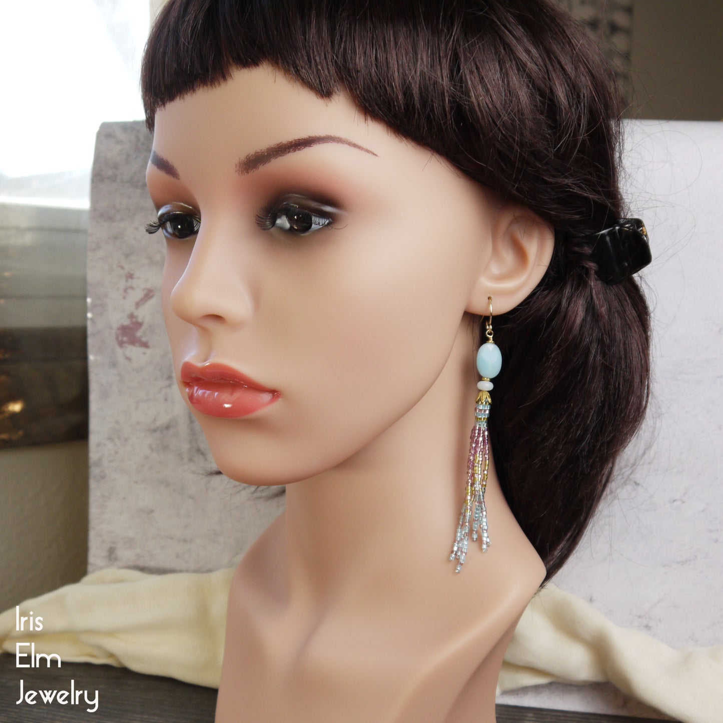 Mannequin head with a stylish pink, gold, and blue amazonite stone and seed bead fringe tassel earring on a neutral background