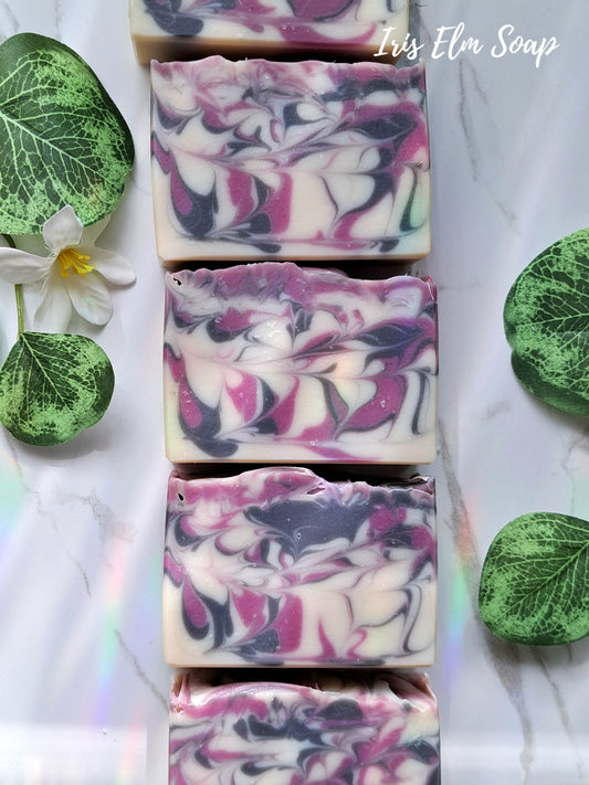 Swirl-patterned black raspberry vanilla handmade soap bars with green leaves and a flower on a light background, branded 'Iris Elm Soap'.