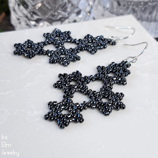 Charcoal grey beaded gothic snowflake earrings on a white surface with 'Iris Elm Jewelry' branding.