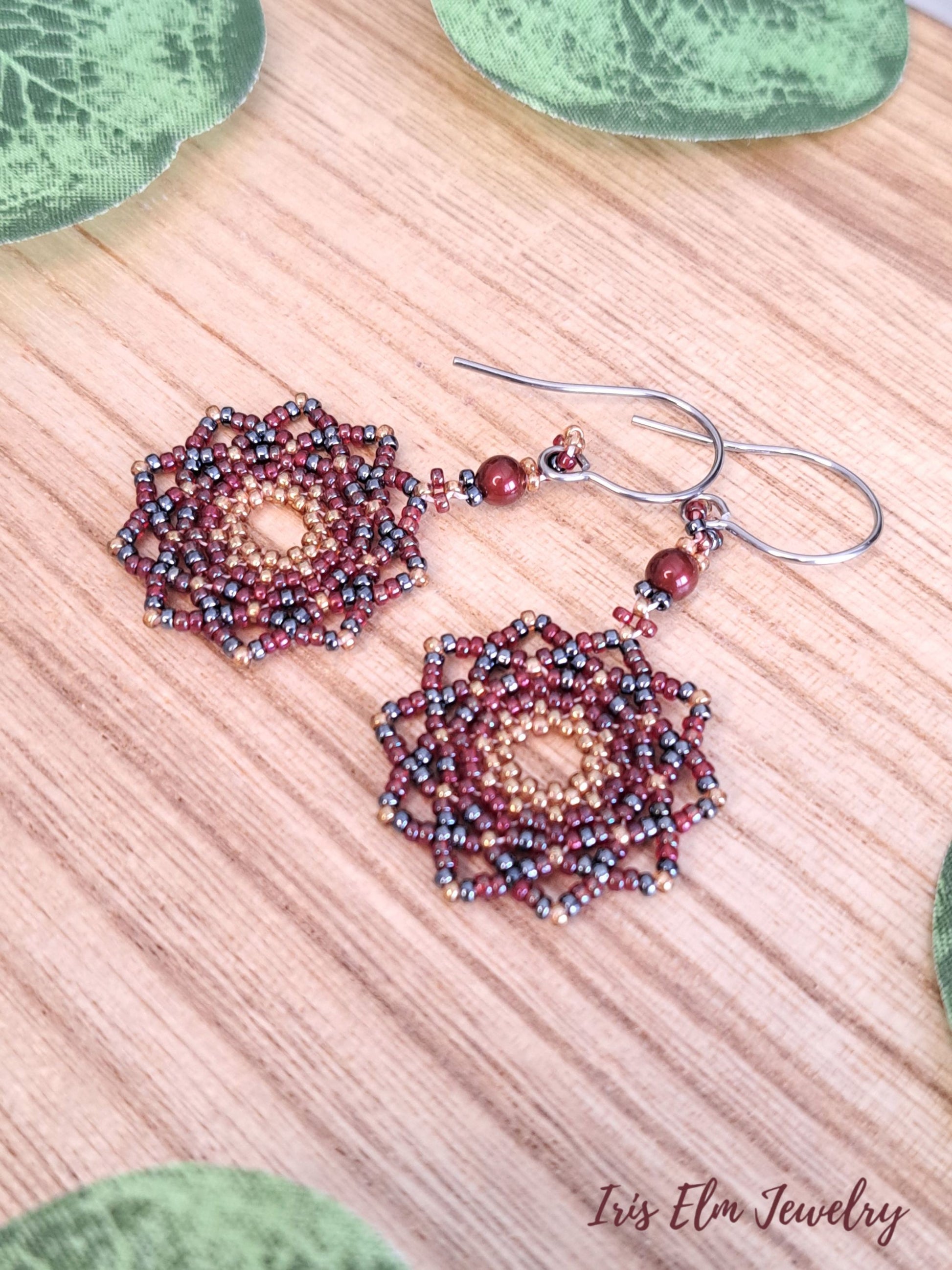 artisan handmade beadwork mandala earrings with red seed beads on wooden surface. Iris Elm Jewelry