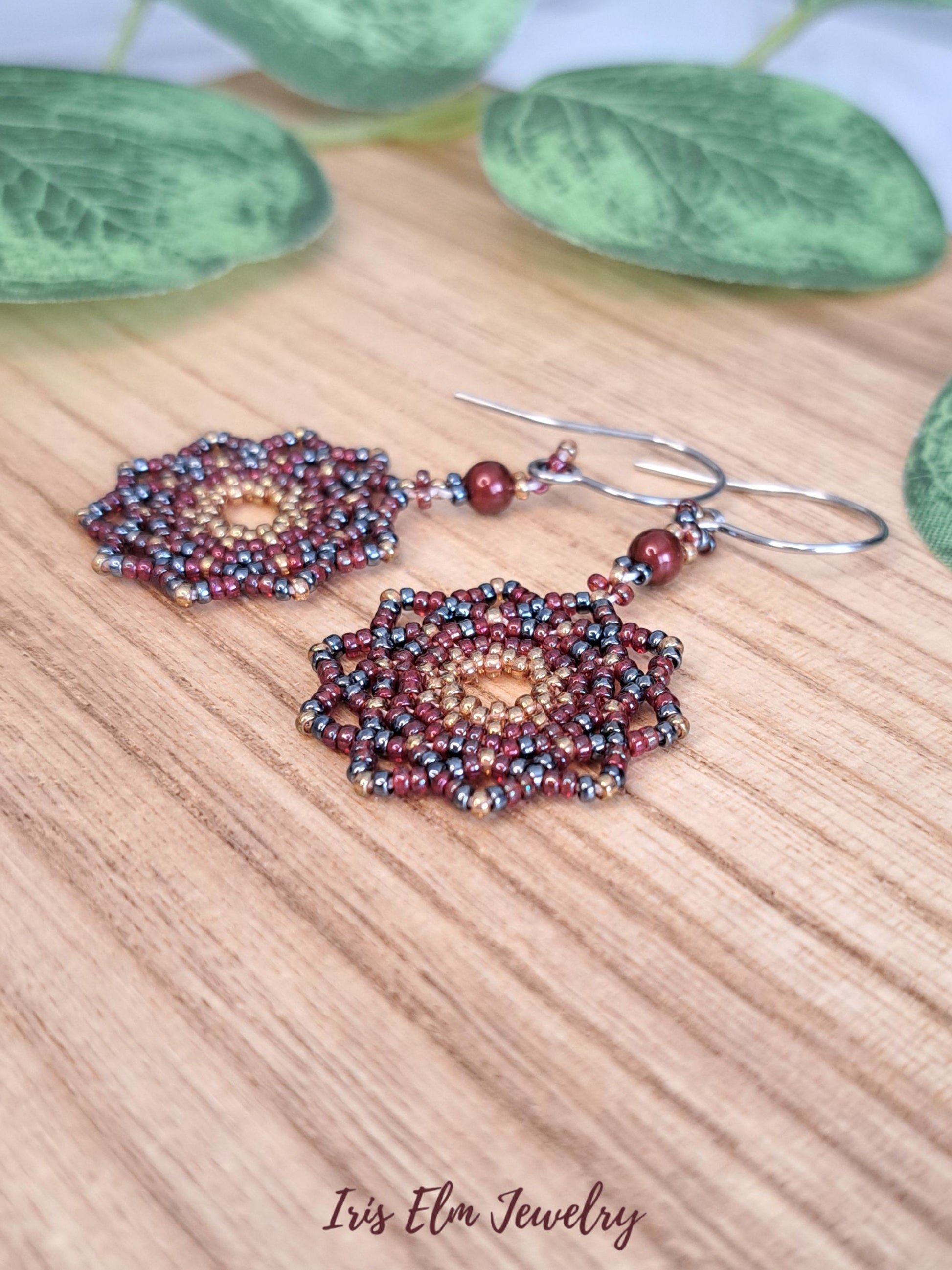 Beaded handcrafted seed bead mandala dangle earrings on a wooden surface with 'Iris Elm Jewelry' branding.